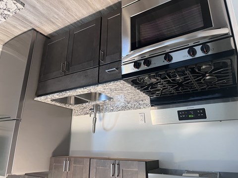 A modern kitchen with a stainless steel oven and microwave above a granite countertop.