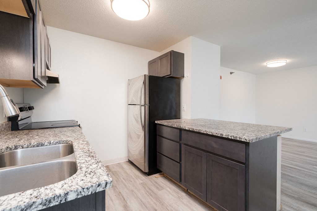 an empty kitchen with granite counter tops and a stainless steel refrigerator