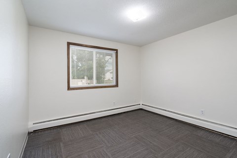 a bedroom with white walls and wood flooring and a window
