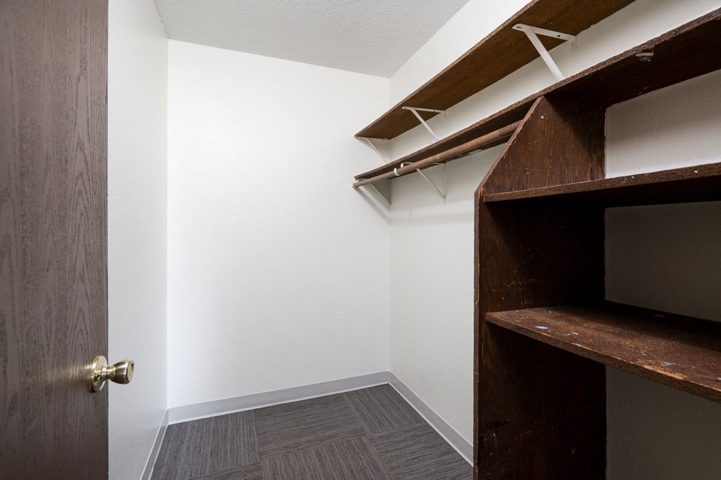 a walk in closet with a wooden closet door and a white wall with a shelf