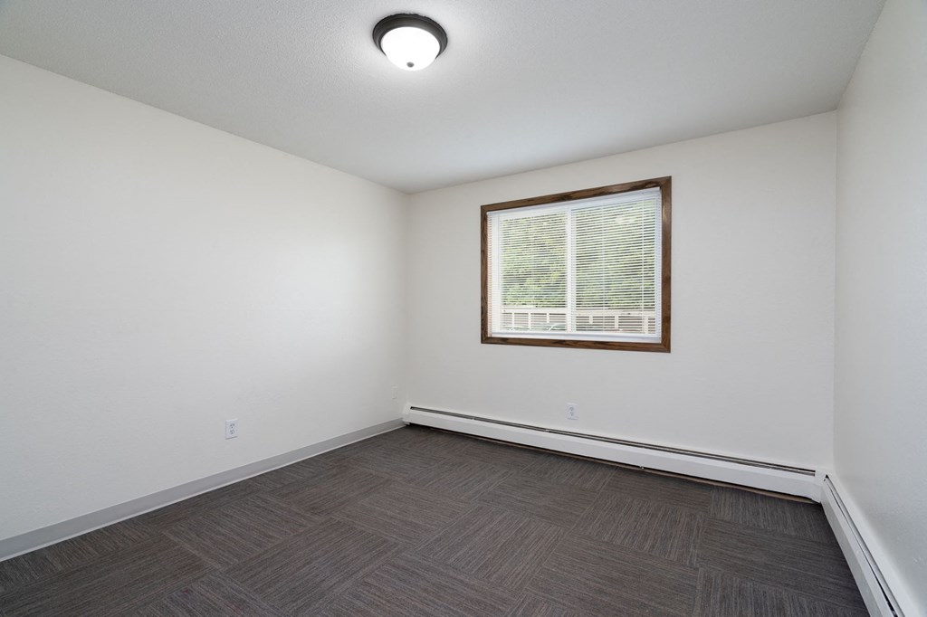 the living room of an empty home with a window and wood flooring