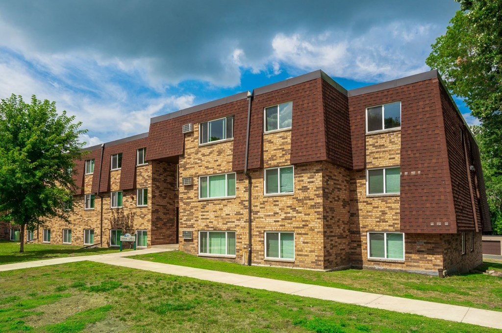 a brick apartment building with green grass and a sidewalk