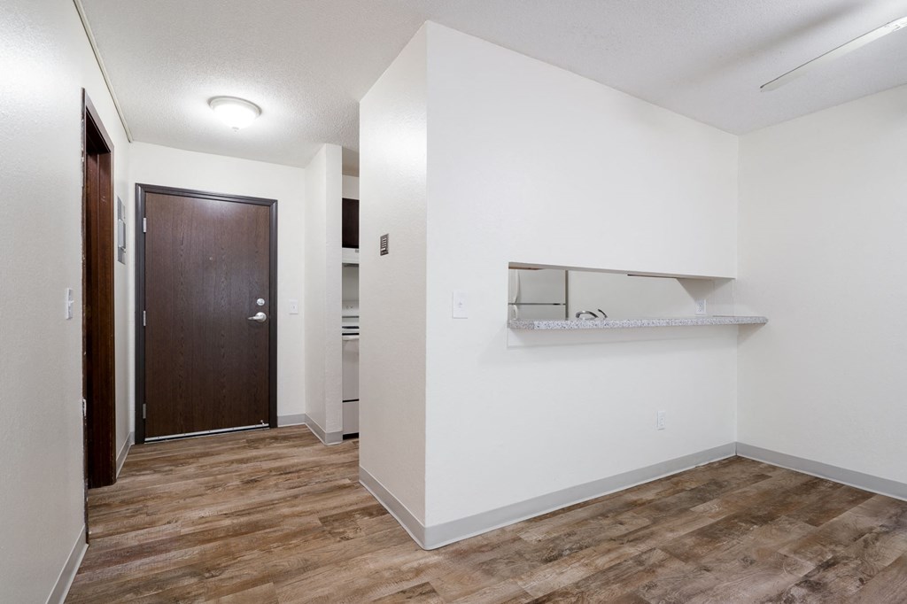 a room with white walls and wood flooring and a door to a bathroom