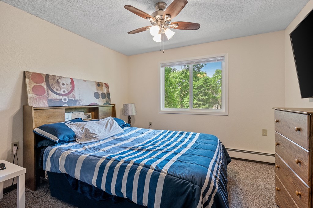 the master bedroom has a king sized bed and a ceiling fan