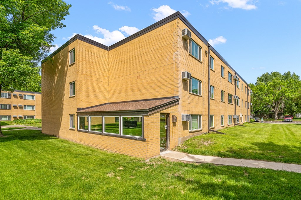 the exterior of a brick building with green grass and trees