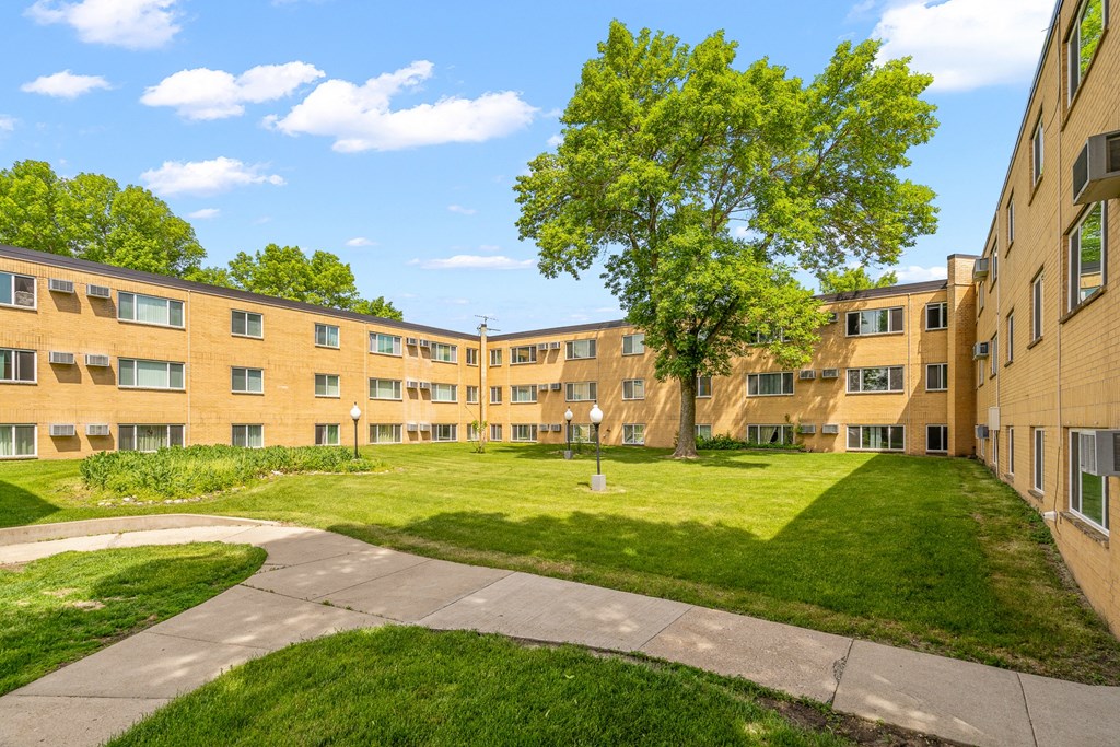 an exterior view of an apartment building with a green lawn and sidewalk