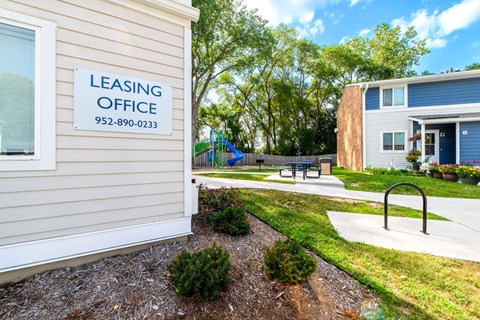 A leasing office sign is on a building with a playground in the background.