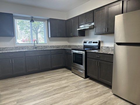 A kitchen with black cabinets and a stainless steel refrigerator.