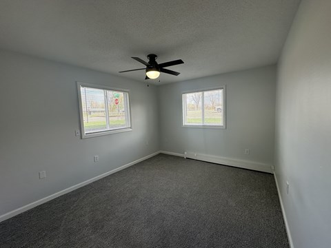 A room with a ceiling fan and two windows.