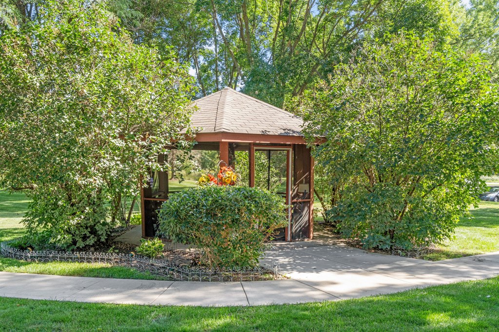a gazebo in a garden with trees and a sidewalk