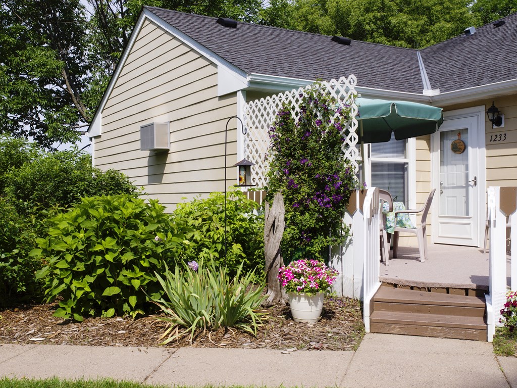 the side of a house with a porch and a pathway with plants and flowers
