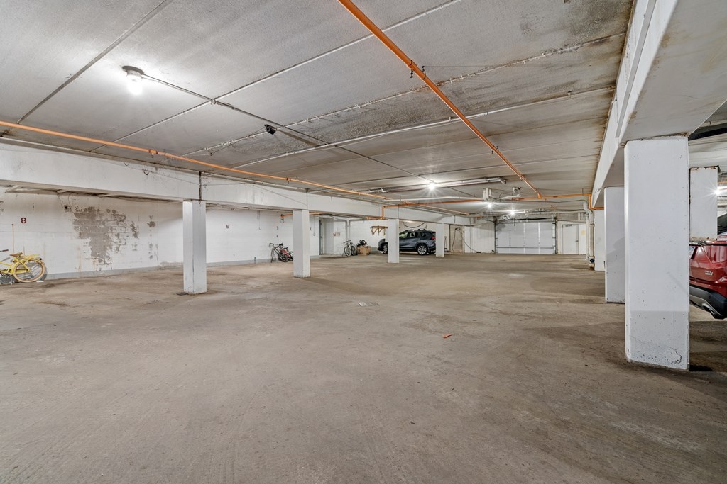 a large parking garage with white pillars and a red car in the distance