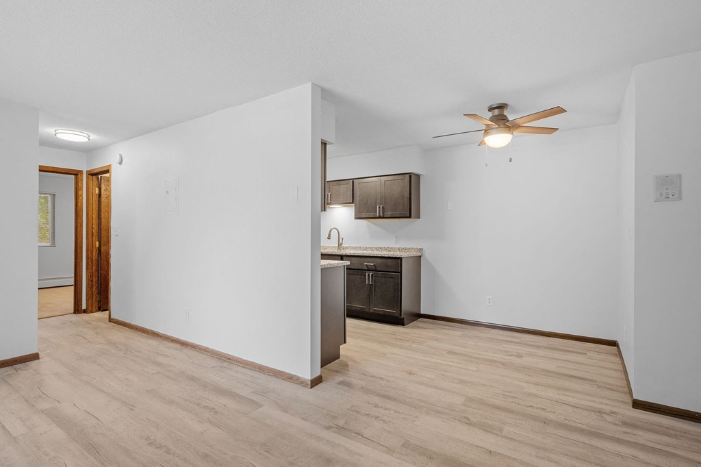 the living room and kitchen of a home with white walls and wood flooring