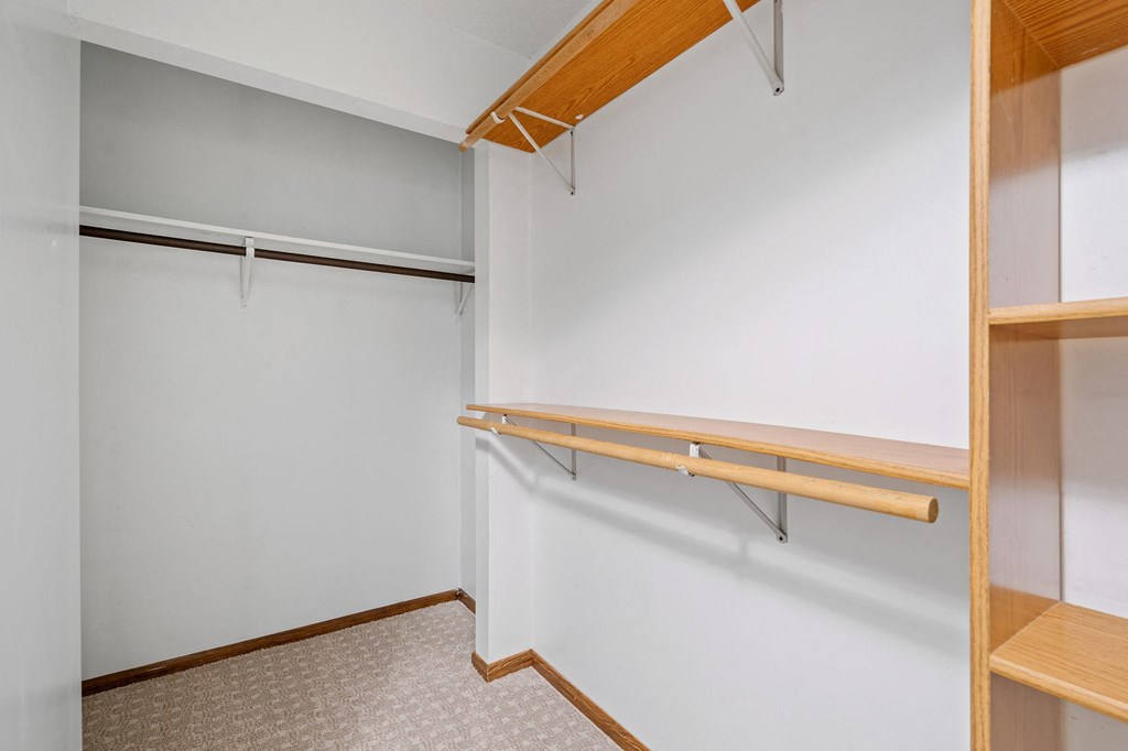 a walk in closet with a white wall and wooden shelves