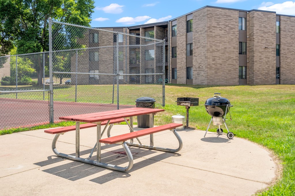 a picnic table in front of a tennis court with a fence