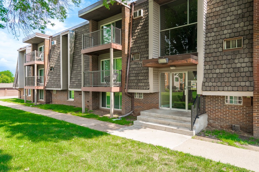 an exterior view of a brick apartment building with a sidewalk and grass