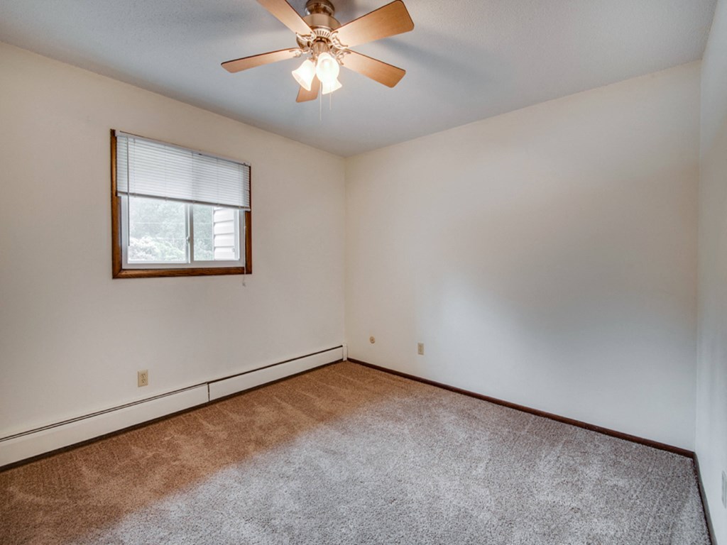the living room of an empty home with carpet and a ceiling fan