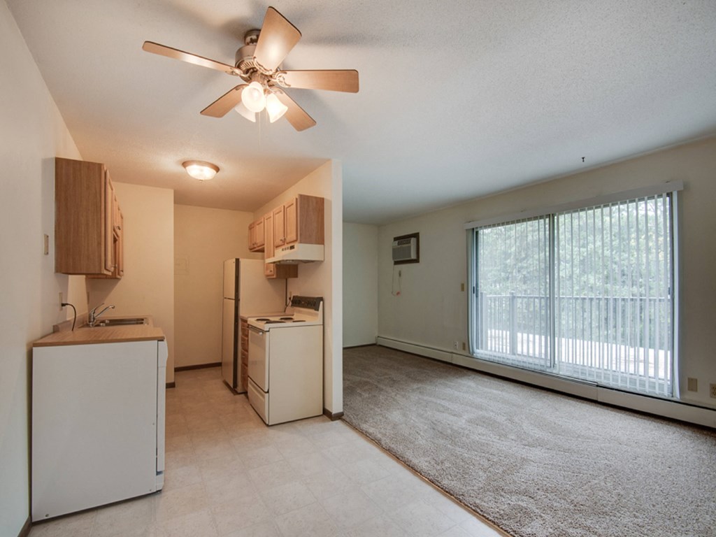 the spacious living room and kitchen with a large window and a ceiling fan