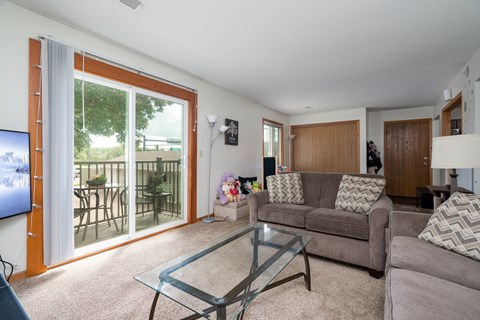 A living room with a glass coffee table and a grey couch.