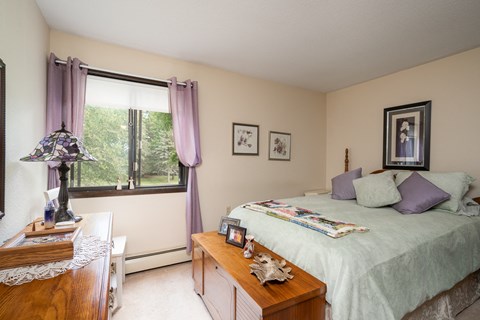A bedroom with a bed, nightstand, and a window with purple curtains.