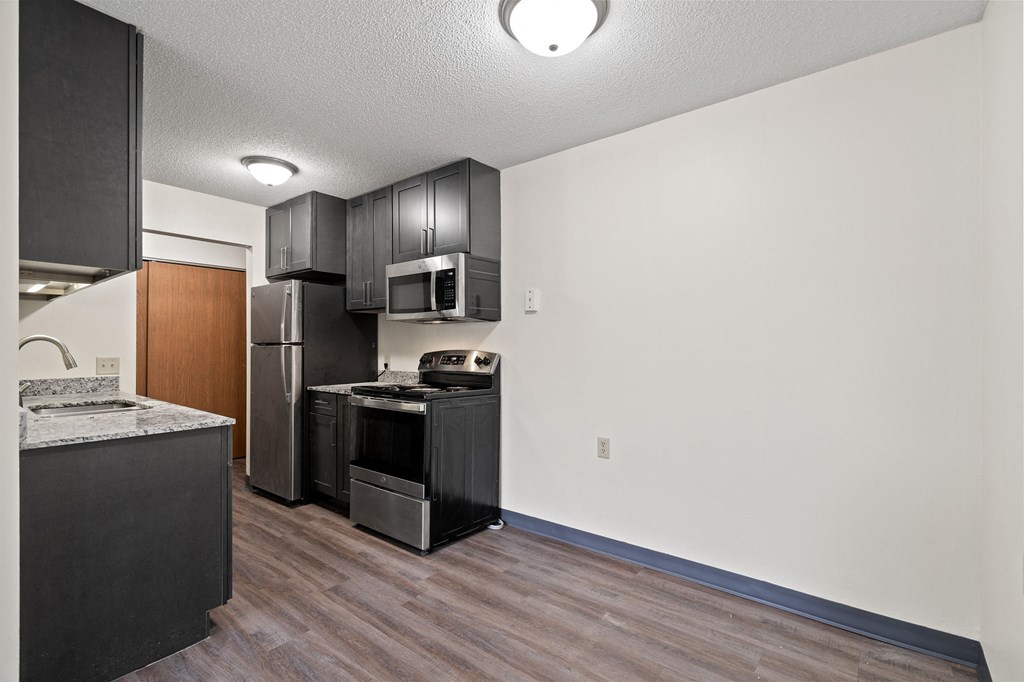 a kitchen with black appliances and white walls and wood flooring