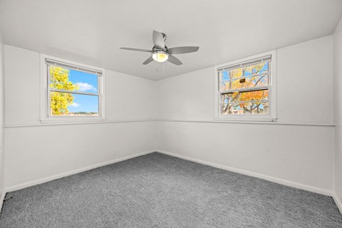 A room with a ceiling fan and two windows.