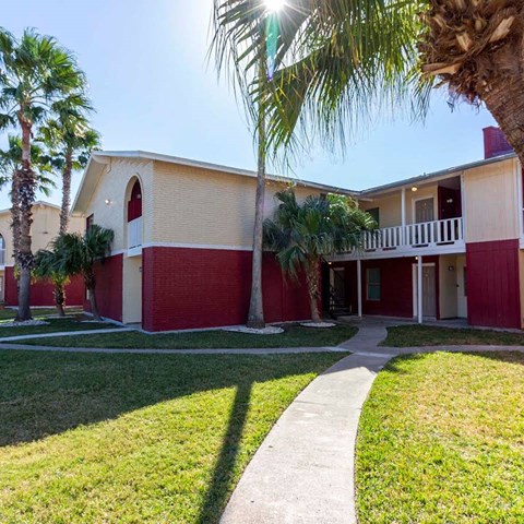 A red and beige building with a white fence and palm trees in front.