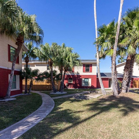 A red building with a white fence and palm trees in front.
