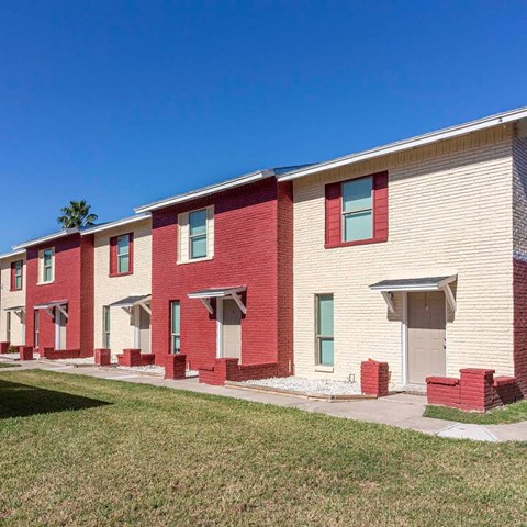 A row of red and white houses with green lawns in front.