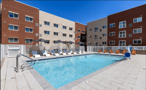 A swimming pool on a patio with sun loungers and a building in the background.