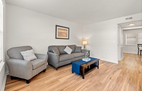 A living room with a grey couch, a grey armchair, a blue coffee table, and a painting on the wall.
