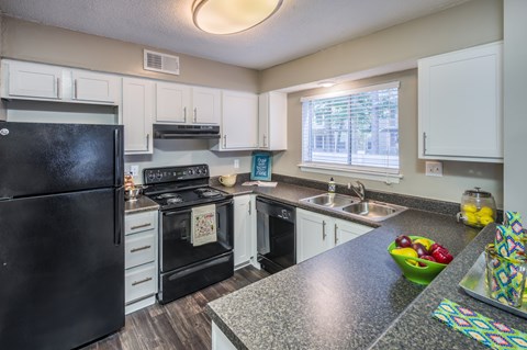 A black refrigerator is in a kitchen with white cabinets.