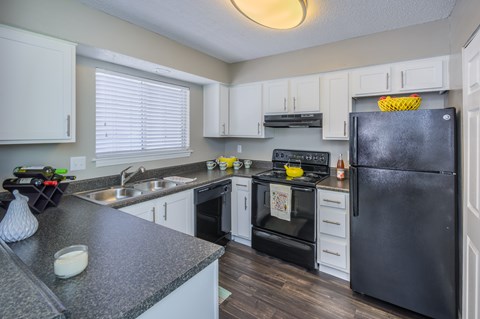 A black refrigerator is in a kitchen with white cabinets.