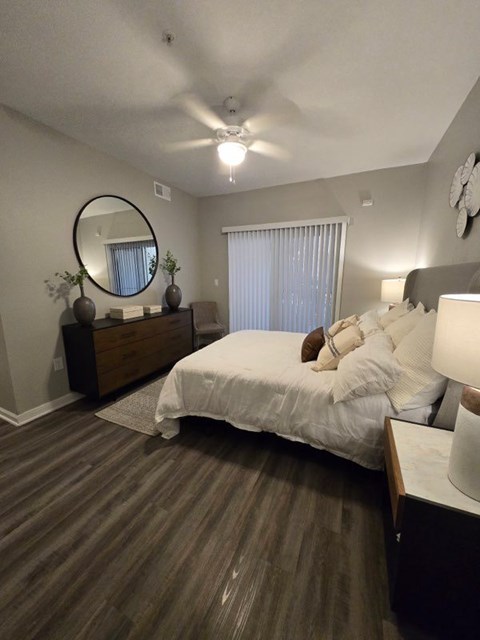 A bedroom with a bed, nightstand, and a round mirror on the wall.