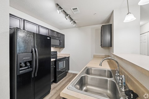 A black fridge and oven in a kitchen with a stainless steel sink.