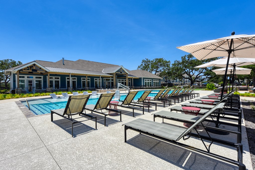 a pool with chairs and umbrellas and a building in the background at Estraya Boerne, Boerne, TX