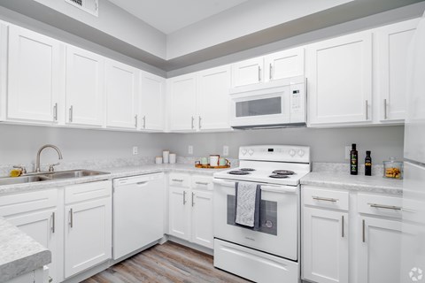 A white kitchen with a stove, sink, and cabinets.