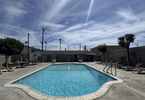A large outdoor swimming pool with lounge chairs and a building in the background.
