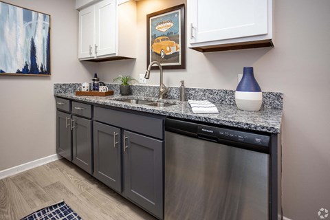 A kitchen with a black dishwasher and grey cabinets.