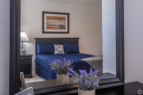 A bedroom with a blue bedspread and a framed picture on the wall.
