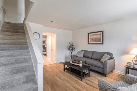 A living room with a grey couch and a staircase.