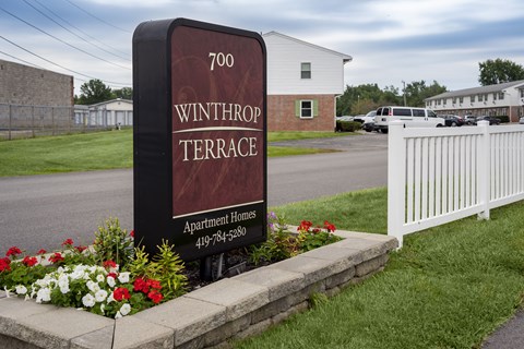 A sign for Winthrop Terrace Apartment Homes stands in front of a white fence.