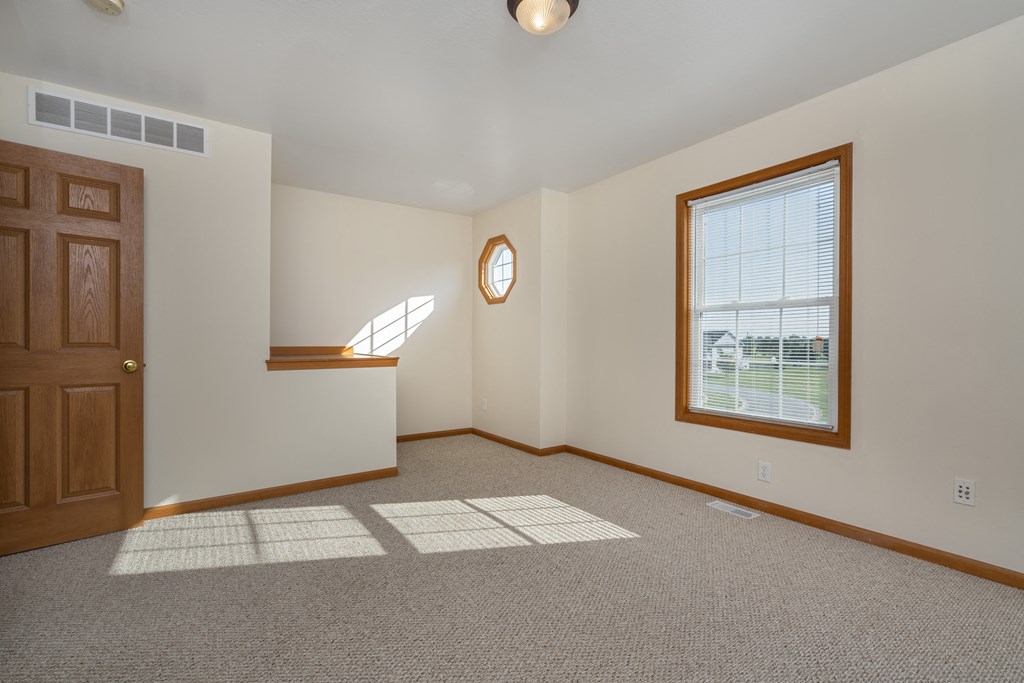 A room with a brown door, a window with blinds, and a round mirror on the wall.