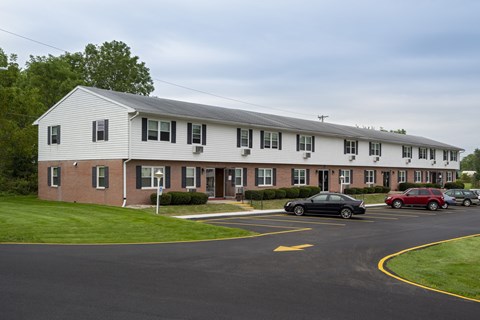 A black car is parked in a parking lot in front of a white building.