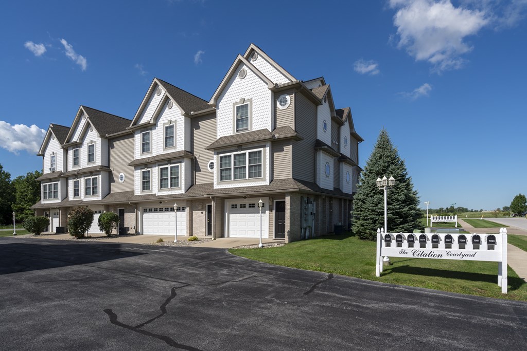 A large, multi-story building with a white sign in front that reads "The Colonial Woods.".