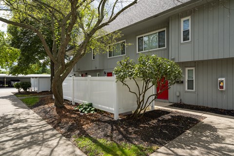 A grey building with a red door and a white fence.