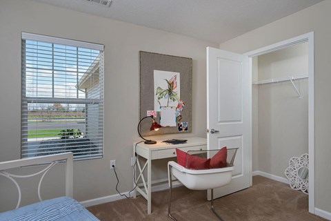 A room with a desk, chair, and a window with blinds.