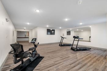 a gym with two exercise machines and a tv on the wall at 41 North Senior Living Apartments, Fort Wayne