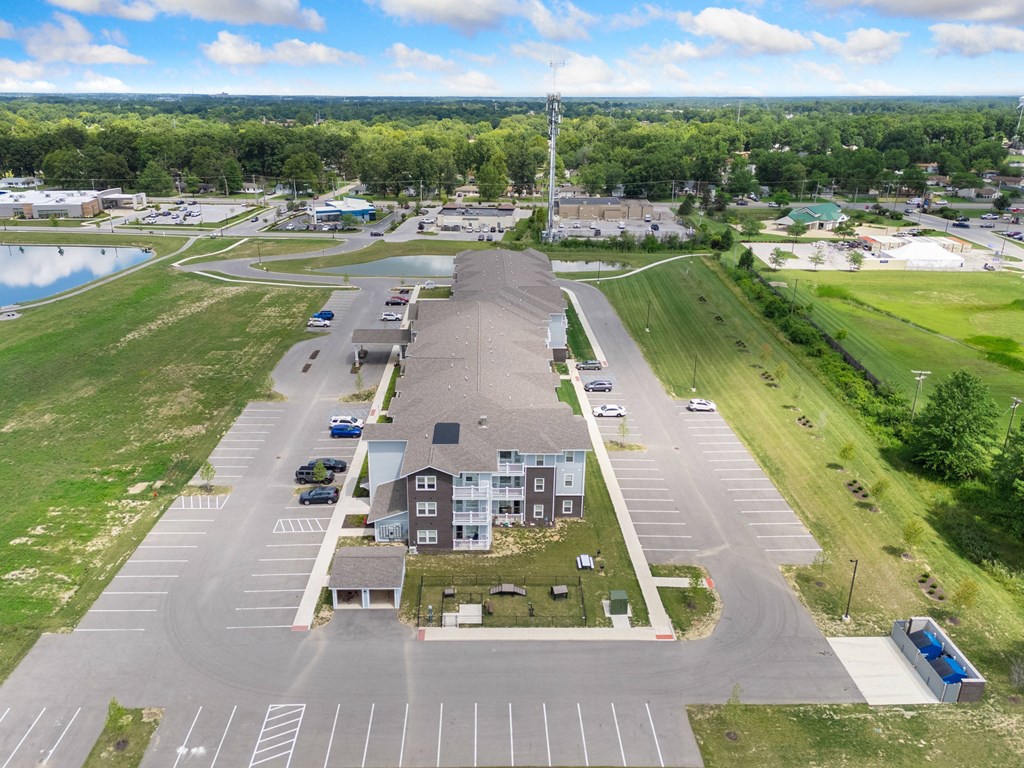 an aerial view of a parking lot with a building and a field and a lake at 41 North Apartments, Indiana, 46835