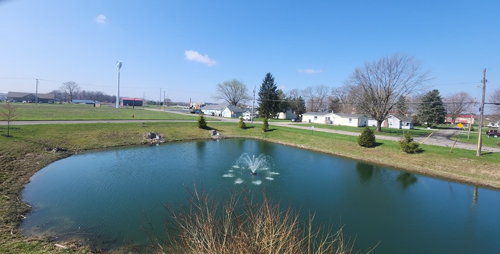 A small pond in the middle of a grassy field with a fountain in the center.